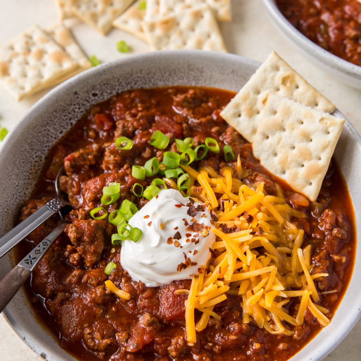 A large bowl of no bean chili topped with chives, cheddar cheese, sour cream, and crackers.